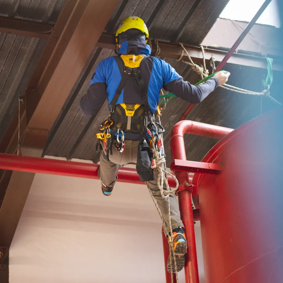 Technician in a yellow helmet ascending ropes beside a red industrial railing
